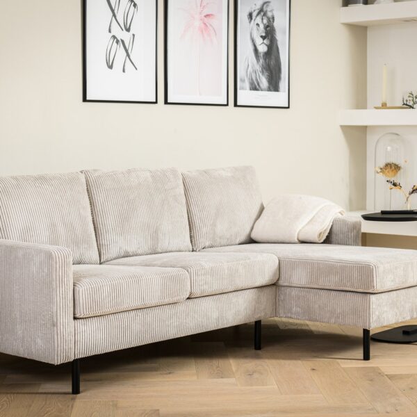 Een 3-zitsbank CL L+R, stof RIB, RIB920 naturel staat in een moderne woonkamer met een ingelijste muurschildering, witte planken en een klein zwart bijzettafeltje met een kussen.
