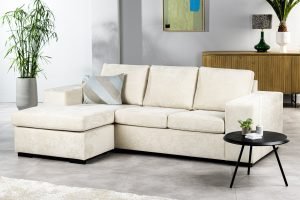 Moderne woonkamer met de 3-zitsbank CL L+R in H460 beige Hotel Chique-stof, gecombineerd met een gestreept kussen, een zwarte ronde bijzettafel met planten, een houten dressoir, groene planten en abstracte wandkunst in een neutrale, minimalistische stijl.