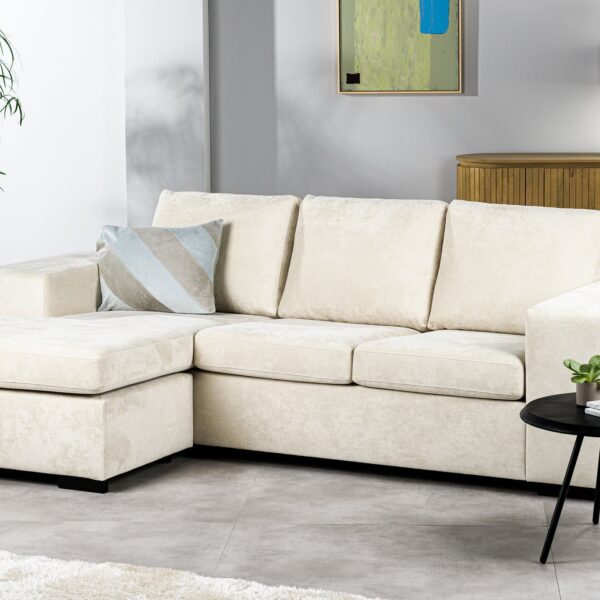 Moderne woonkamer met de 3-zitsbank CL L+R in H460 beige Hotel Chique-stof, gecombineerd met een gestreept kussen, een zwarte ronde bijzettafel met planten, een houten dressoir, groene planten en abstracte wandkunst in een neutrale, minimalistische stijl.