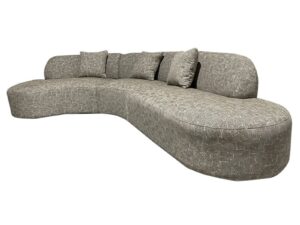 De Amsterdam 2.5 Seater + Ottoman Latte is een ruime, moderne, gebogen beige bank met een structuurafwerking en vier bijpassende sierkussens op de rugleuning.