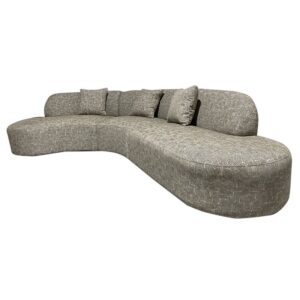 De Amsterdam 2.5 Seater + Ottoman Latte is een ruime, moderne, gebogen beige bank met een structuurafwerking en vier bijpassende sierkussens op de rugleuning.