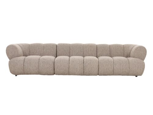 Een lange, moderne beige bank met een zachte, gestructureerde stof. De bank heeft zes grote, ronde kussens die de rugleuning en zitting vormen, wat een gezellige en uitnodigende uitstraling creëert. Hij staat laag bij de grond.