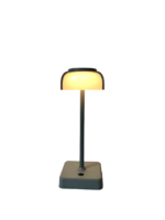 Een moderne minimalistische bureaulamp met een matte grijze basis en een ondoorzichtige geel-witte kap. De lamp gloeit, werpt een warm licht en staat op een vierkante basis met een ronde knop.
