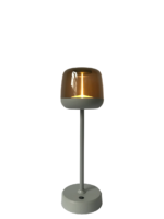 Een moderne tafellamp met een strakke grijze basis en steel, met een cilindrische amberkleurige glazen kap die een warme gloed uitstraalt. De lamp staat op een effen witte achtergrond.
