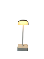 Een kleine, moderne witte tafellamp met een rechthoekige voet staat rechtop. Het heeft een koepelvormige kap, zacht gloeiend, bevestigd aan een slanke, verticale steel.