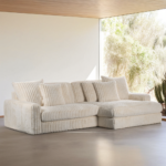 Een moderne woonkamer toont de 3 zits bank CL L+R, stof Vito 23, D460 beige sectionaal met pluche kussens, in de buurt van ramen van vloer tot plafond die een helder woestijnachtig landschap buiten onthullen.
