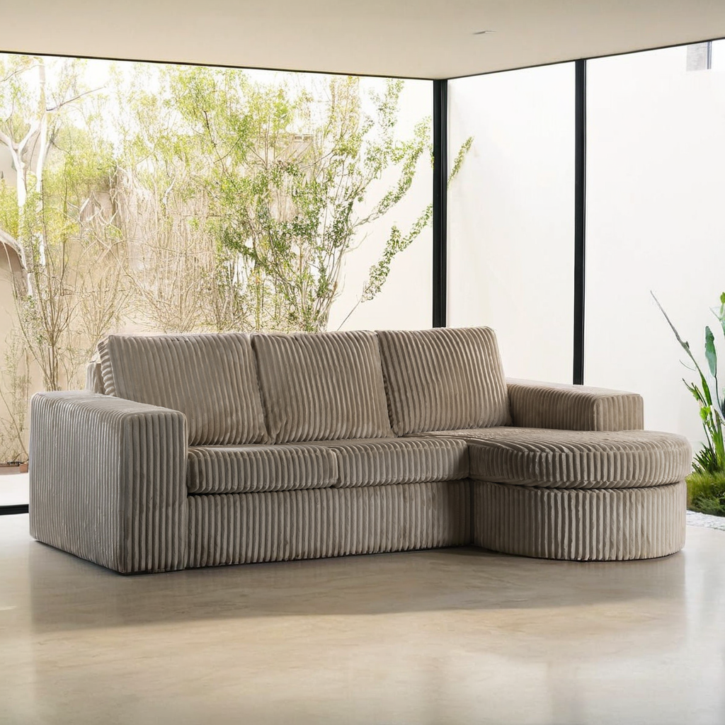 Een 3 zits bank CL L+R in Tillia 03 L460 beige stof staat in een lichte woonkamer met ramen van vloer tot plafond en uitzicht op groen buiten.