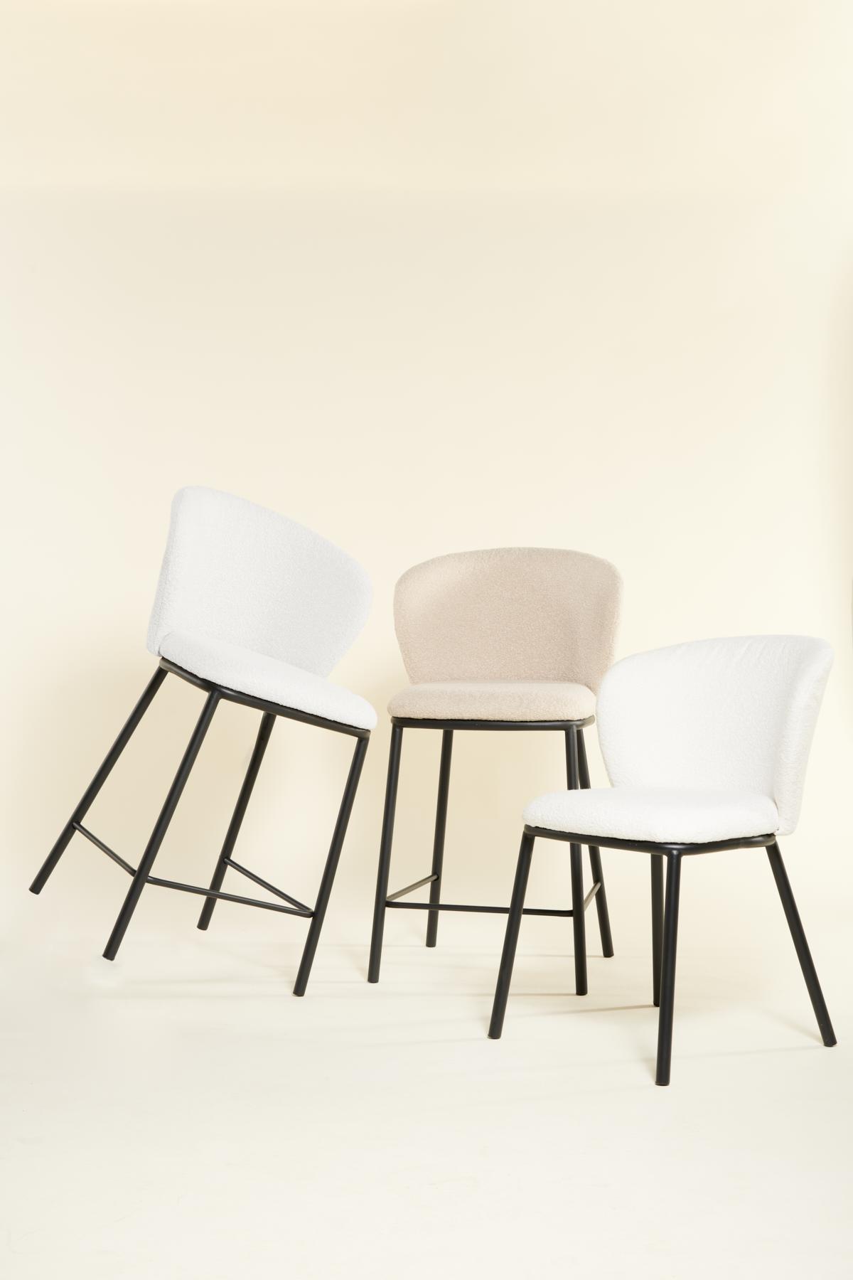 Drie moderne stoelen met zwarte poten staan opgesteld tegen een lichtbeige achtergrond. Twee stoelen zijn bekleed met wit en één met beige. De stoelen hebben een strak, minimalistisch design.