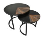 Twee ronde in elkaar passende tafels met zwarte bovenkanten en metalen poten. Elke tafel heeft een decoratief houten gedeelte in de vorm van een kwartcirkel, wat een vleugje rustieke charme toevoegt. De tafels zijn gepositioneerd met de kleinere gedeeltelijk onder de grotere.