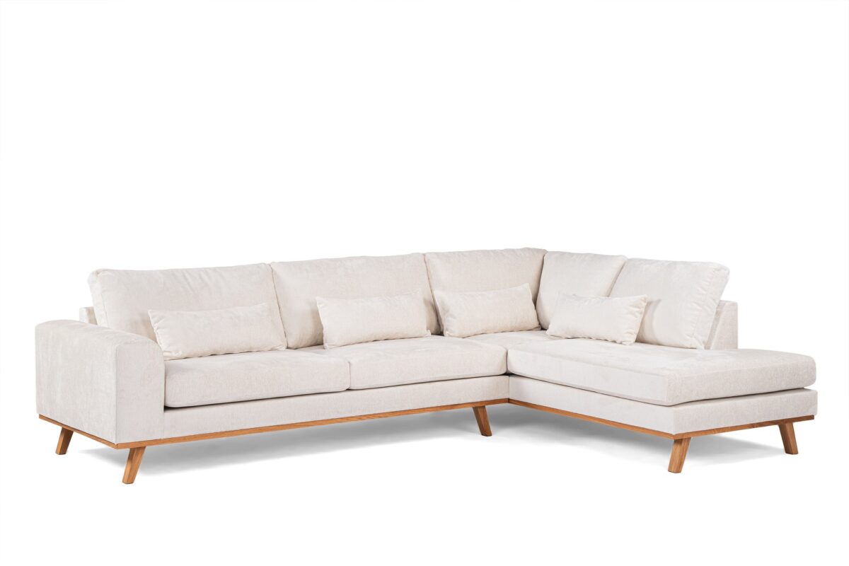 L-vormige sectionele bank met crèmekleurige bekleding en houten poten. De bank heeft strakke lijnen en is versierd met verschillende bijpassende kussens. Het heeft zowel een lang als een kort gedeelte, wat een comfortabele hoekzitopstelling creëert.