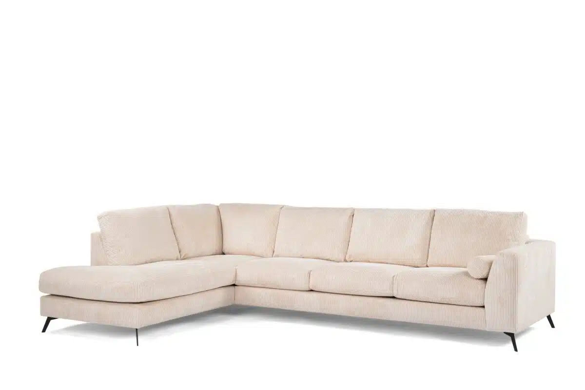 Beige L-vormige sectionele bank op zwarte poten. Met kussens en een chaise longue aan de linkerkant, tegen een witte achtergrond.