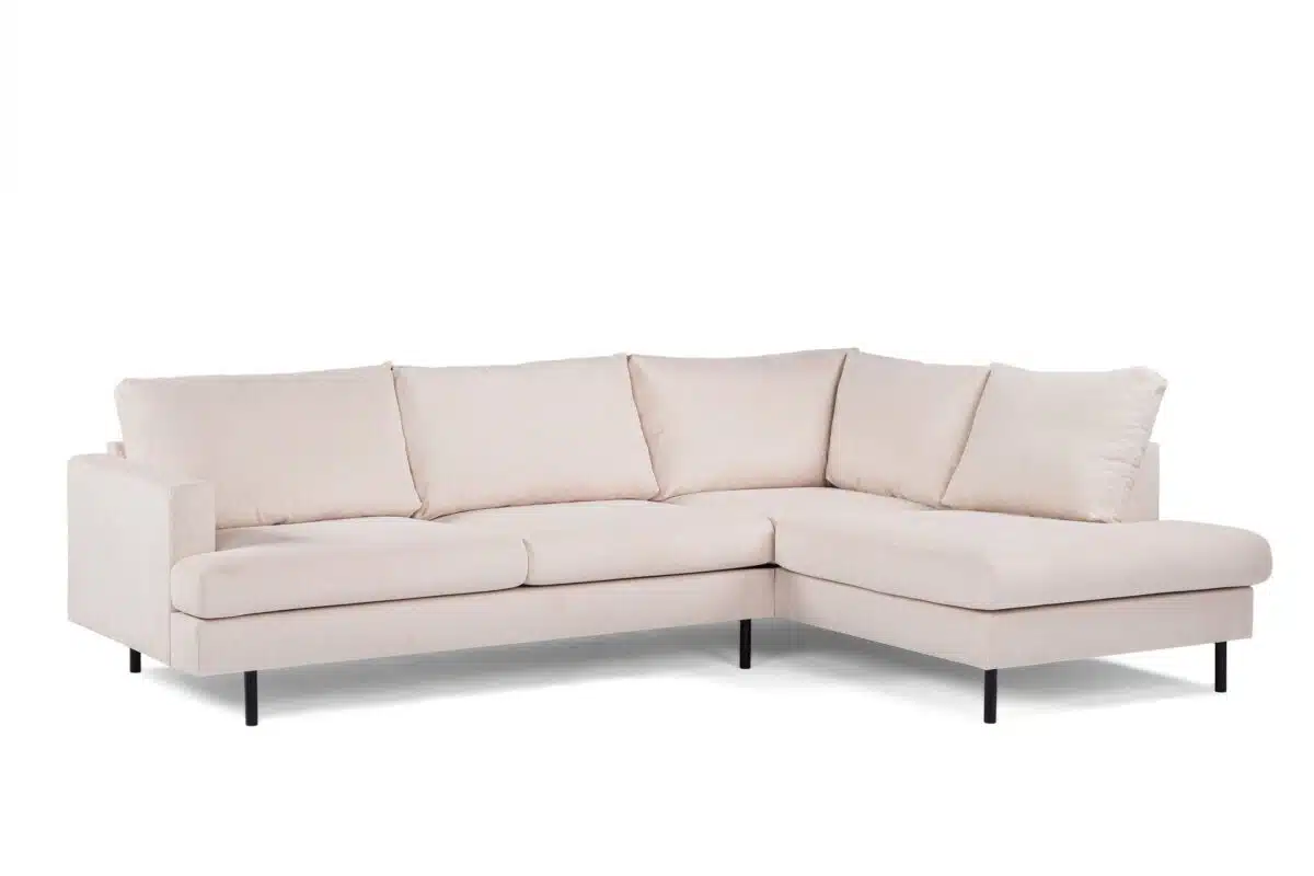 Een lichtbeige, L-vormige sectionele bank met pluche kussens en zwarte poten wordt getoond tegen een witte achtergrond. De bank heeft een modern en minimalistisch design.