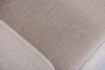 Close-up van een beige stoffen bank die de getextureerde bekleding met fijne, gelijkmatige stiksels laat zien. De afbeelding benadrukt het strakke, geweven patroon en de zachte uitstraling van de stof.