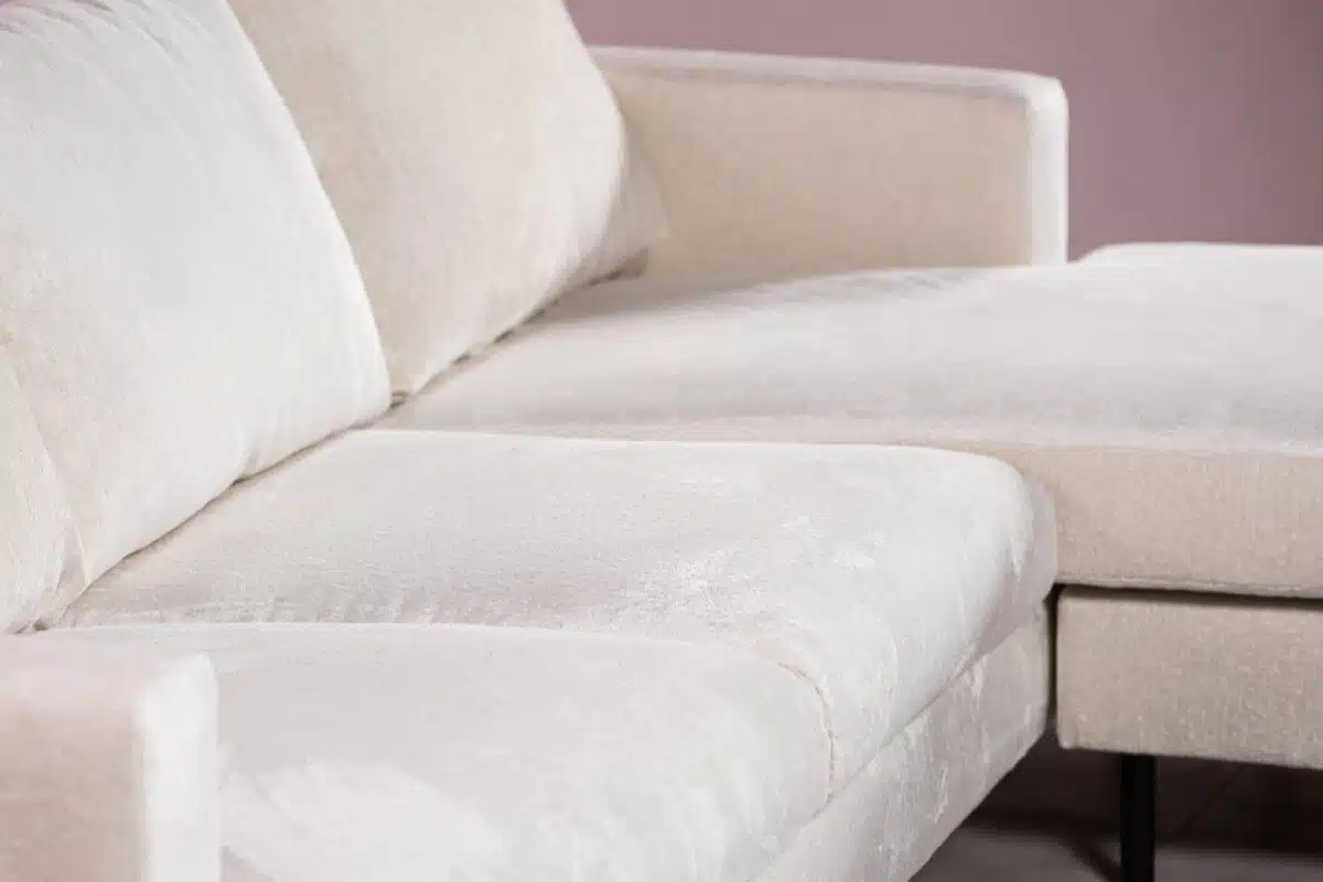 Close-up van een lichtbeige sectionele bank met een zachte stoffen textuur. De bank staat tegen een gedempte roze muur, wat een minimalistische en gezellige sfeer creëert.