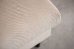 Close-up van een beige, geribbelde stoffen bankarm, die de textuur en subtiele rondingen van de bekleding benadrukt. De achtergrond is zacht vervaagd, wat de ingewikkelde ontwerpdetails van de bank benadrukt.