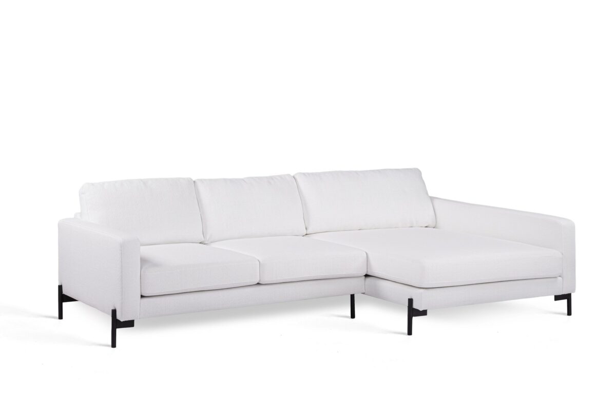 Een moderne witte sectionele bank met drie rugkussens en een verlengde chaise longue aan de rechterkant. Het heeft strakke lijnen en zwarte metalen poten, tegen een witte achtergrond.