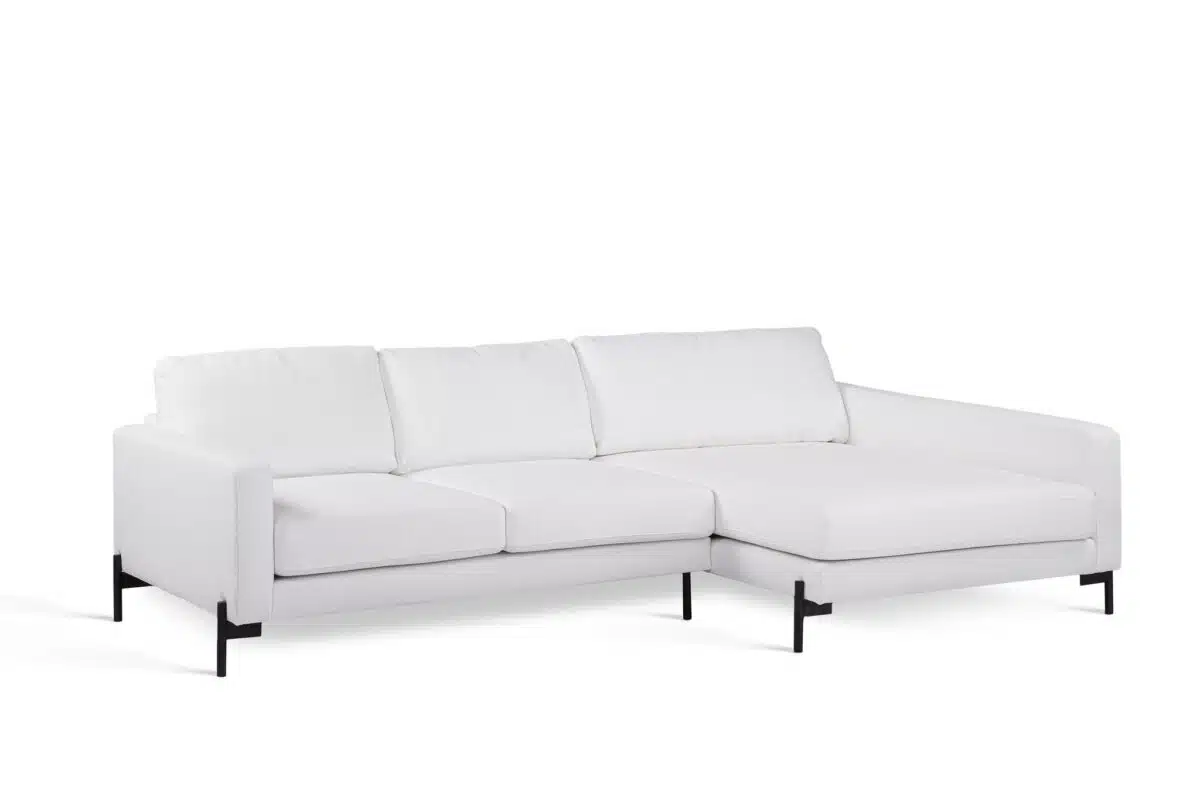 Een moderne witte sectionele bank met drie rugkussens en een verlengde chaise longue aan de rechterkant. Het heeft strakke lijnen en zwarte metalen poten, tegen een witte achtergrond.