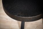 Close-up van de Salontafel rond 74 cm in B341 vintage zwart, met een rond zwart tafelblad met structuur en zwarte poten op een lichte houten vloer.