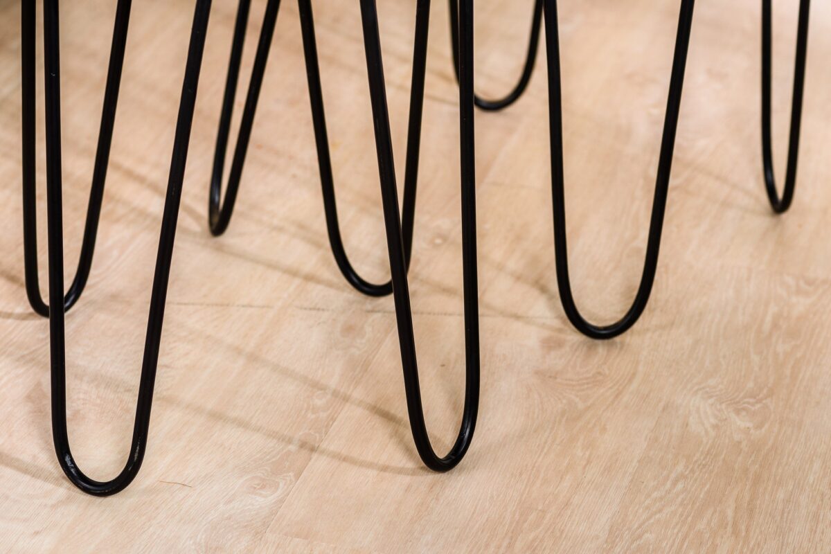 Close-up van een aantal zwarte metalen haarspeldpoten uit de Salontafel, set van 2, A340 zwart op een lichte houten vloer, die gebogen lijnen en schaduwen vormen.