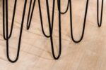 Close-up van een aantal zwarte metalen haarspeldpoten uit de Salontafel, set van 2, A340 zwart op een lichte houten vloer, die gebogen lijnen en schaduwen vormen.