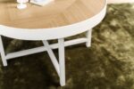De Salontafel rond 74 cm, Lennox, L350 eiken heeft een lichtbruine ronde bovenkant en witte poten, die op een groen vloerkleed staan met een paar witte decoratieve items die gedeeltelijk zichtbaar zijn.