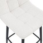 Close-up van een gewatteerde zitting met een gecapitonneerde, getextureerde lichte stoffen bekleding. De zitting heeft metalen poten met een donkere afwerking. Het ontwerp is modern en minimalistisch.
