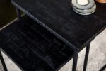 Close-up van een zwarte, gestructureerde nesttafelset met drie keramische kommen op het bovenoppervlak. De tafels hebben een matte afwerking en staan op een lichtgekleurd tapijt.