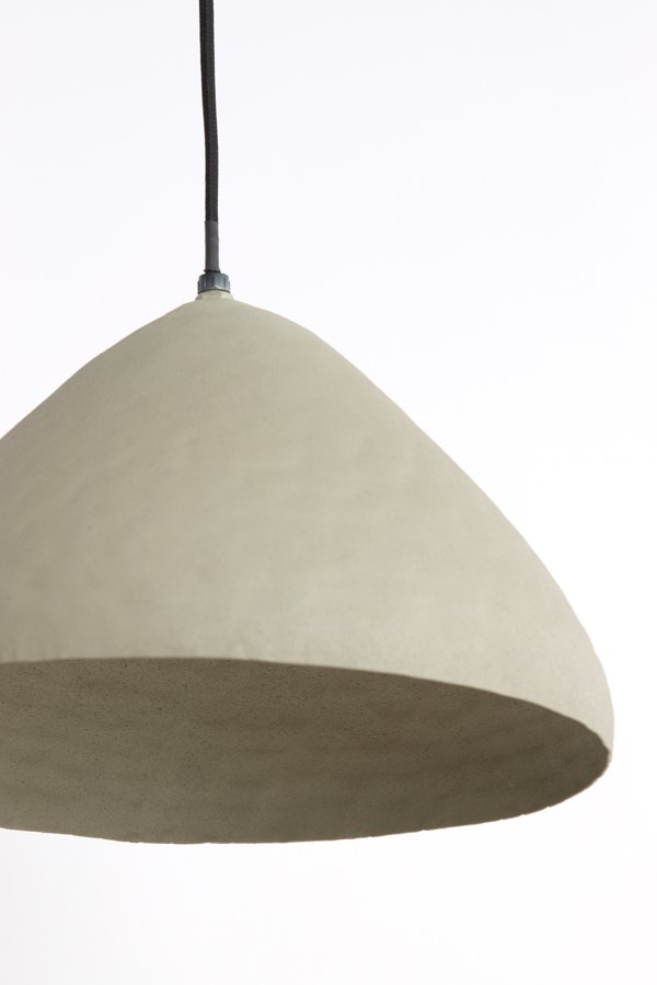 Een minimalistische, koepelvormige hanglamp met een glad oppervlak hangt aan een zwart snoer tegen een witte achtergrond. De lampenkap lijkt gemaakt te zijn van een lichtgekleurd materiaal, misschien beton of keramiek.