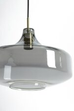 Een moderne hangende hanglamp met een rookgrijze glazen kap en een metalen armatuur hangt aan een zwarte kabel. De lamp is strak en reflecterend, en werpt subtiele schaduwen en highlights op het gladde oppervlak.