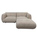 Een moderne, lichtbruine sectionele bank met een textuurstof afwerking. De bank heeft een lage rugleuning en ronde armleuningen, met een chaise longue aan de rechterkant. Hij rust op kleine, nauwelijks zichtbare poten.