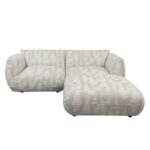 Een moderne, pluche L-vormige sectionele bank met lichtbeige, patroonstof. Het heeft brede armleuningen en een chaise longue-extensie, wat een stijlvolle en comfortabele zitopstelling biedt voor een moderne woonkamer.
