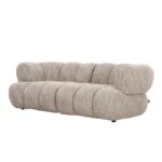 Een moderne, beige stoffen bank met een pluche, afgerond design en gecapitonneerde details, met drie ruime kussens. De bank heeft een laag profiel en lijkt comfortabel, rustend op subtiele zwarte poten.