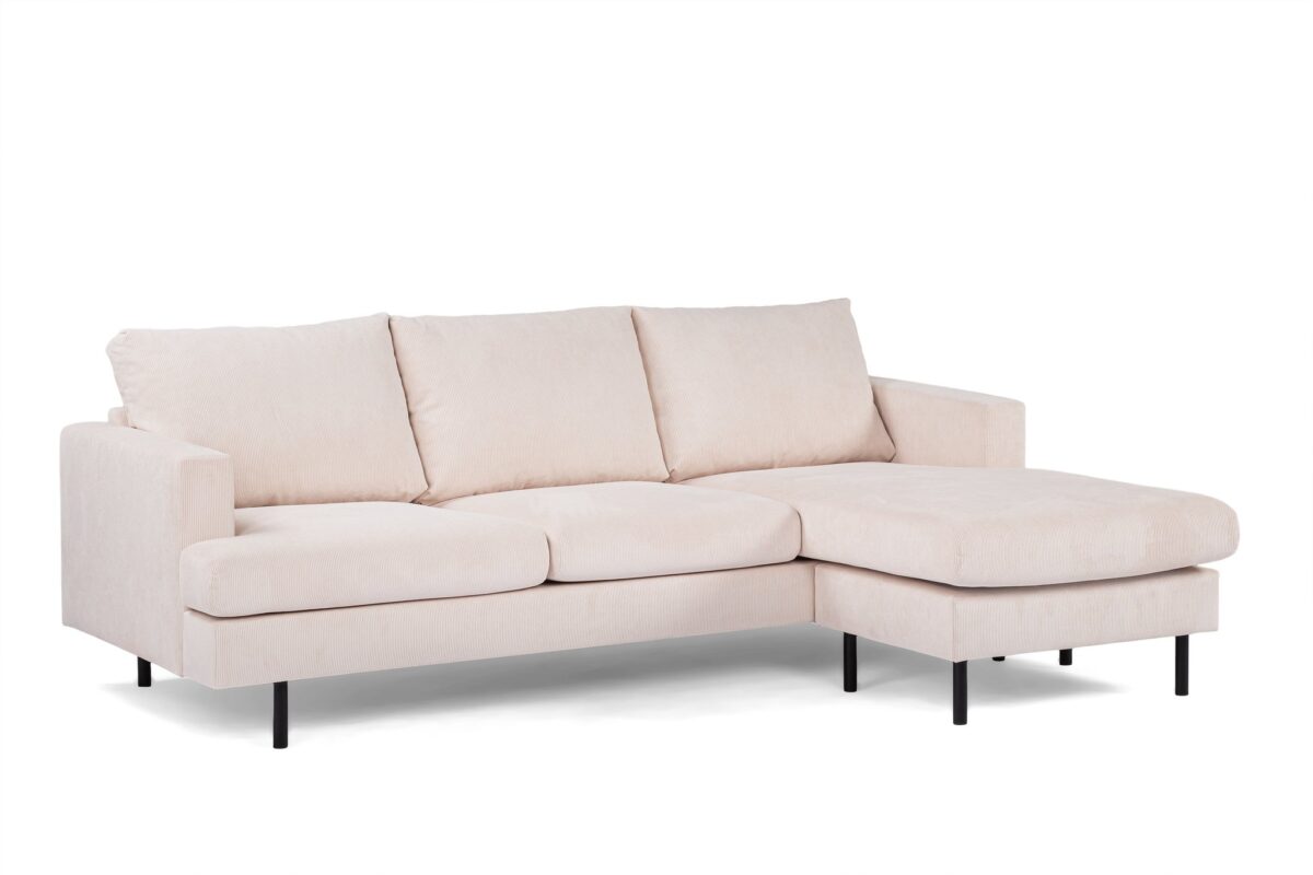 Een moderne beige sectionele bank met drie kussens en een chaise longue aan de rechterkant. Het heeft eenvoudige, rechte lijnen en zwarte metalen poten, tegen een witte achtergrond.