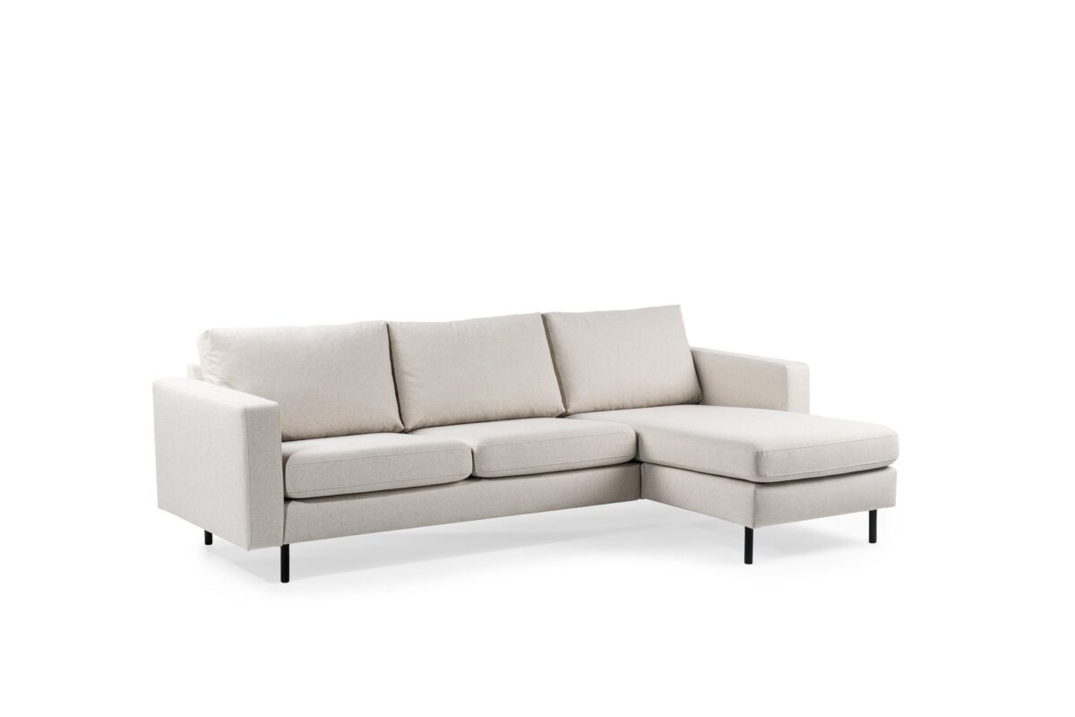 De 3 zits bank CL L+R in Dillon D820 ivoor stof is een modern lichtbeige sectionaal met drie zit- en rugkussens, een chaise lounge aan de rechterkant en zwarte metalen poten, getoond op een witte achtergrond.