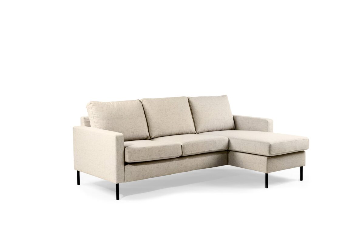 Een beige, moderne sectionele bank met drie rugkussens en een chaise longue aan de rechterkant. Het heeft strakke lijnen en wordt ondersteund door slanke zwarte metalen poten, tegen een effen witte achtergrond.
