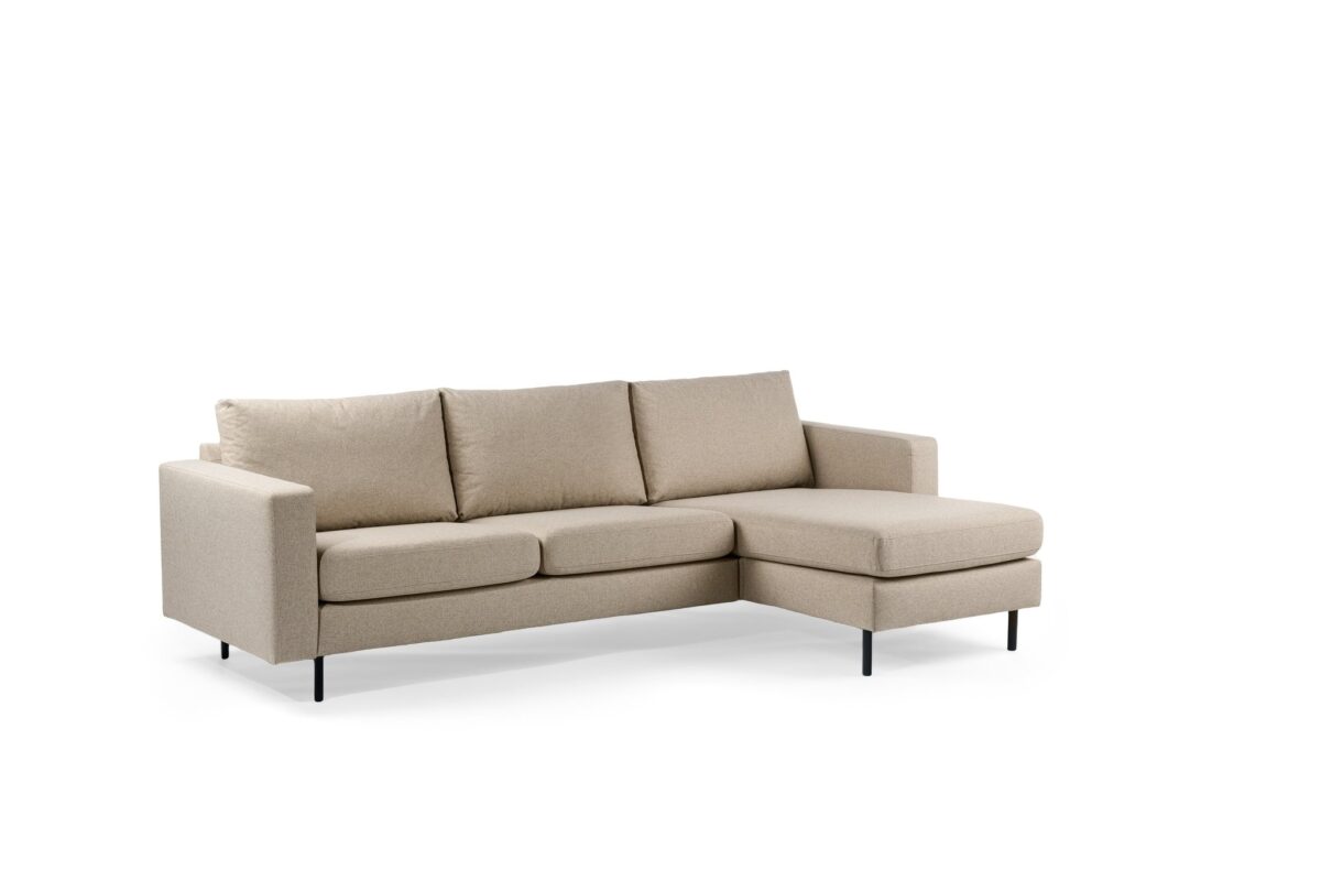 Een beige sectionele bank met drie zitkussens en een chaise longue aan de rechterkant, tegen een effen witte achtergrond. De bank heeft een minimalistisch design met rechte lijnen en zwarte poten.