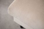 Close-up van een beige stof met een getextureerd, geribbeld patroon dat een meubelstuk bedekt, mogelijk een armleuning van een bank of een stoel. De zachte, neutrale kleur en fijne lijnen creëren een subtiele, elegante uitstraling.
