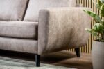 Close-up van de 3 zits bank CL L+R in Savannah S520 taupe stof met zwarte poten op een houten vloer, naast een groene potplant. Lichte houten latten vormen de achtergrondmuur en een licht vloerkleed is gedeeltelijk zichtbaar.