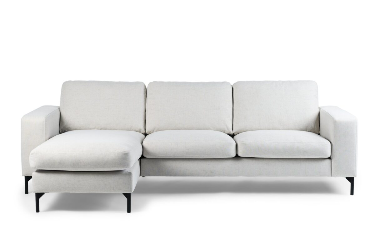 Een moderne, lichtgrijze L-vormige bank met drie zitkussens en een chaise longue aan de linkerkant. Het heeft een minimalistisch design met korte zwarte poten, tegen een witte achtergrond.