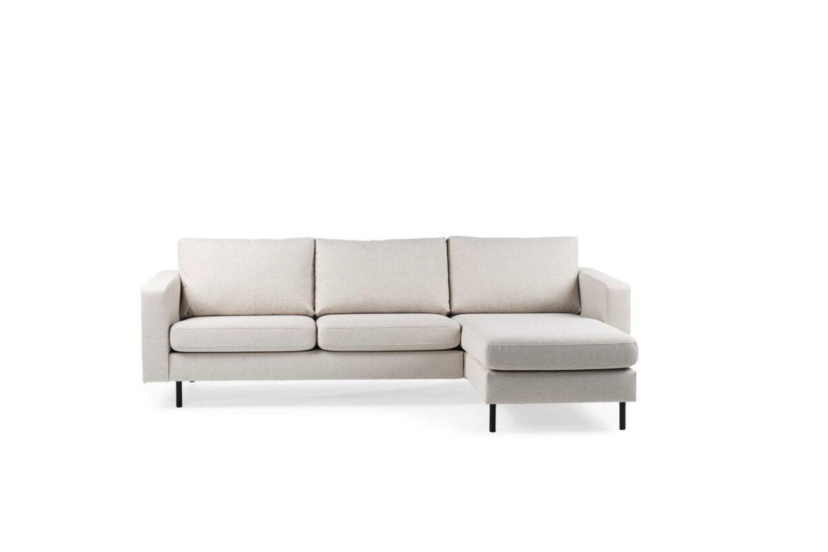 Een lichtgrijze hoekbank met drie zitkussens en een chaise longue aan de rechterkant, ondersteund door zwarte poten, tegen een witte achtergrond.