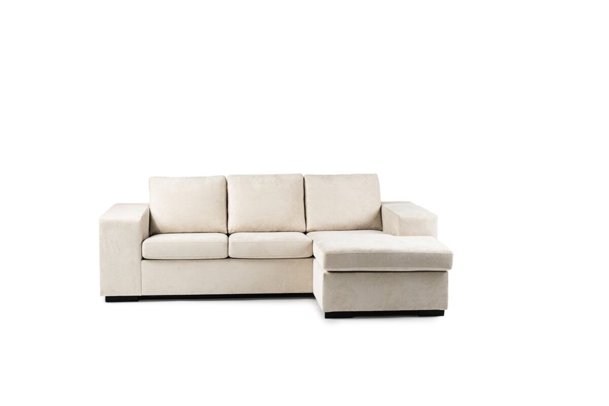 Een beige sectionele bank met drie gestoffeerde zittingen en een chaise longue aan de rechterkant, tegen een effen witte achtergrond. De bank heeft brede armleuningen en staat op korte zwarte poten.
