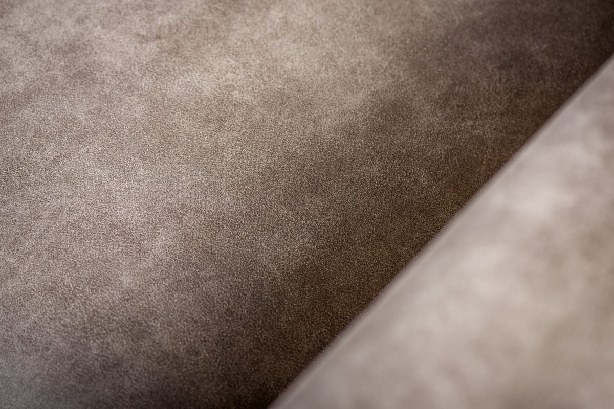 Close-up van de 3 zits bank CL L+R in Savannah stof, S520 taupe: het gladde, zachte lichtbruine suède-achtige oppervlak heeft subtiele naden en zachte schaduwen, die de getextureerde en gezellige uitstraling benadrukken.