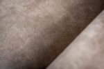Close-up van de 3 zits bank CL L+R in Savannah stof, S520 taupe: het gladde, zachte lichtbruine suède-achtige oppervlak heeft subtiele naden en zachte schaduwen, die de getextureerde en gezellige uitstraling benadrukken.