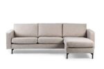 Een moderne, lichtbeige sectionele bank met drie kussens en een chaise longue aan de rechterkant. De bank heeft rechte armleuningen en zwarte metalen poten op een witte achtergrond.