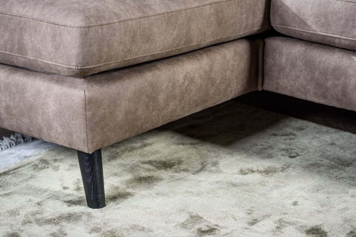 Close-up van de hoek van de 3 zits bank CL L+R, bekleed met Savannah S520 taupe stof met een suède-achtige textuur en zwarte poten, getoond op een zacht, licht grijs-beige tapijt.