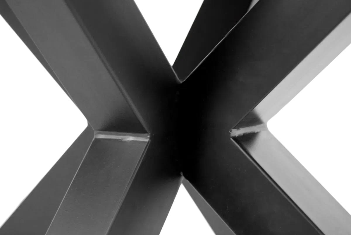 Close-up van een modern, zwart metalen tafelpootontwerp, in de vorm van een "X" met scherpe hoeken en strakke lijnen, tegen een witte achtergrond.