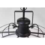 Close-up van een zwarte plafondventilator in industriële stijl met metalen kooiontwerp. De centrale naaf en bladen van de ventilator zijn zichtbaar, wat een minimalistische en moderne esthetiek laat zien tegen een lichte achtergrond.