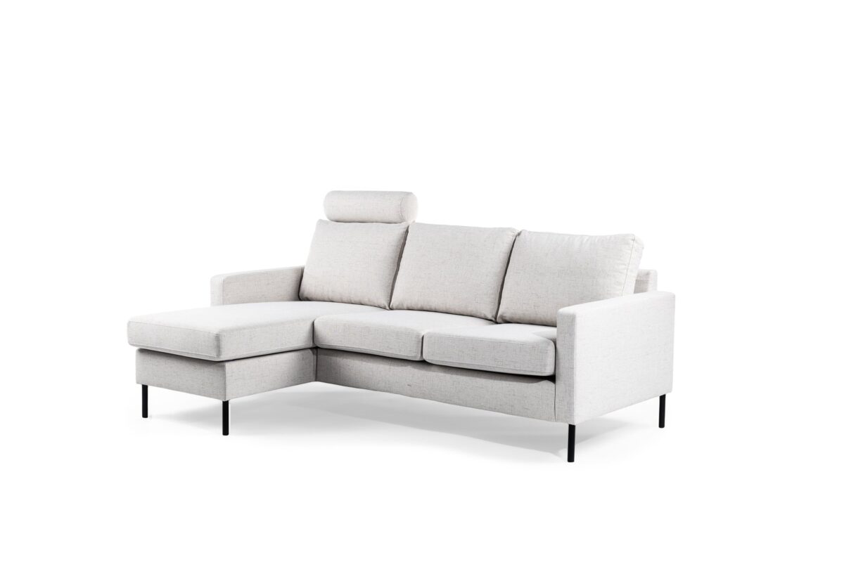 Een moderne, lichtgrijze sectionele bank met een chaise longue aan de linkerkant, drie kussens en slanke zwarte poten. Het heeft een minimalistisch ontwerp en een afneembare hoofdsteun. De bank staat tegen een effen witte achtergrond.