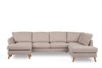 Een lichtbeige L-vormige sectionele bank met houten poten. De bank heeft vijf gestoffeerde zitplaatsen en een chaise longue aan de linkerkant, tegen een effen witte achtergrond.