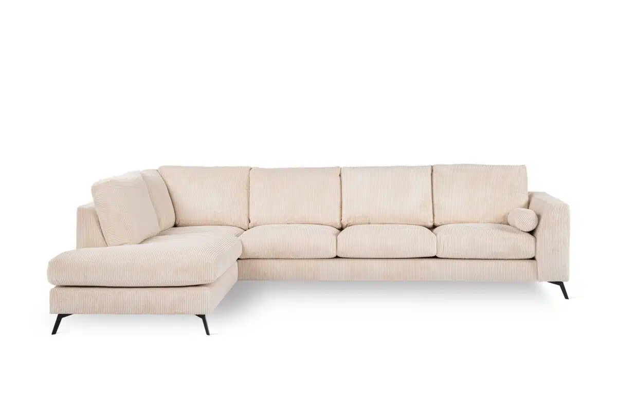 Een grote, lichtbeige sectionele bank met een chaise longue aan de linkerkant. De bank heeft een strak, modern design met slanke zwarte poten en wordt geleverd met een bijpassend rond sierkussen.